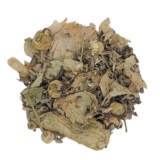 Dried herbal tea blend with dried flowers, leaves, and roots piled in a round off-white ceramic bowl on a white background.
